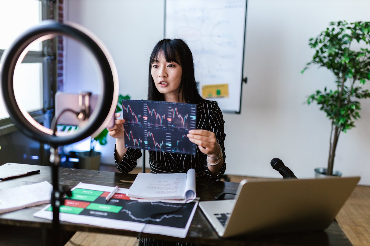 A woman vlogger discusses stock market trends using charts in a home studio.